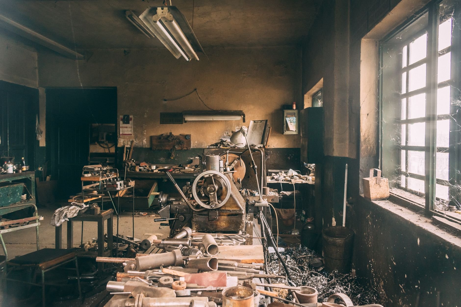 Rustic industrial workshop filled with vintage machinery, tools, and metal parts in a dimly lit room