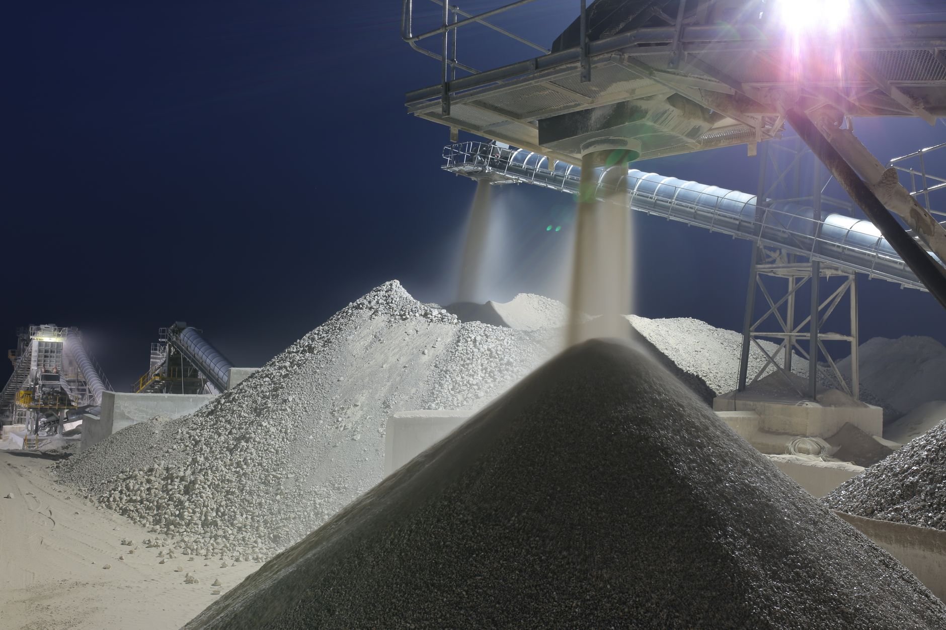 Nighttime industrial processing site with machinery and heaps of material