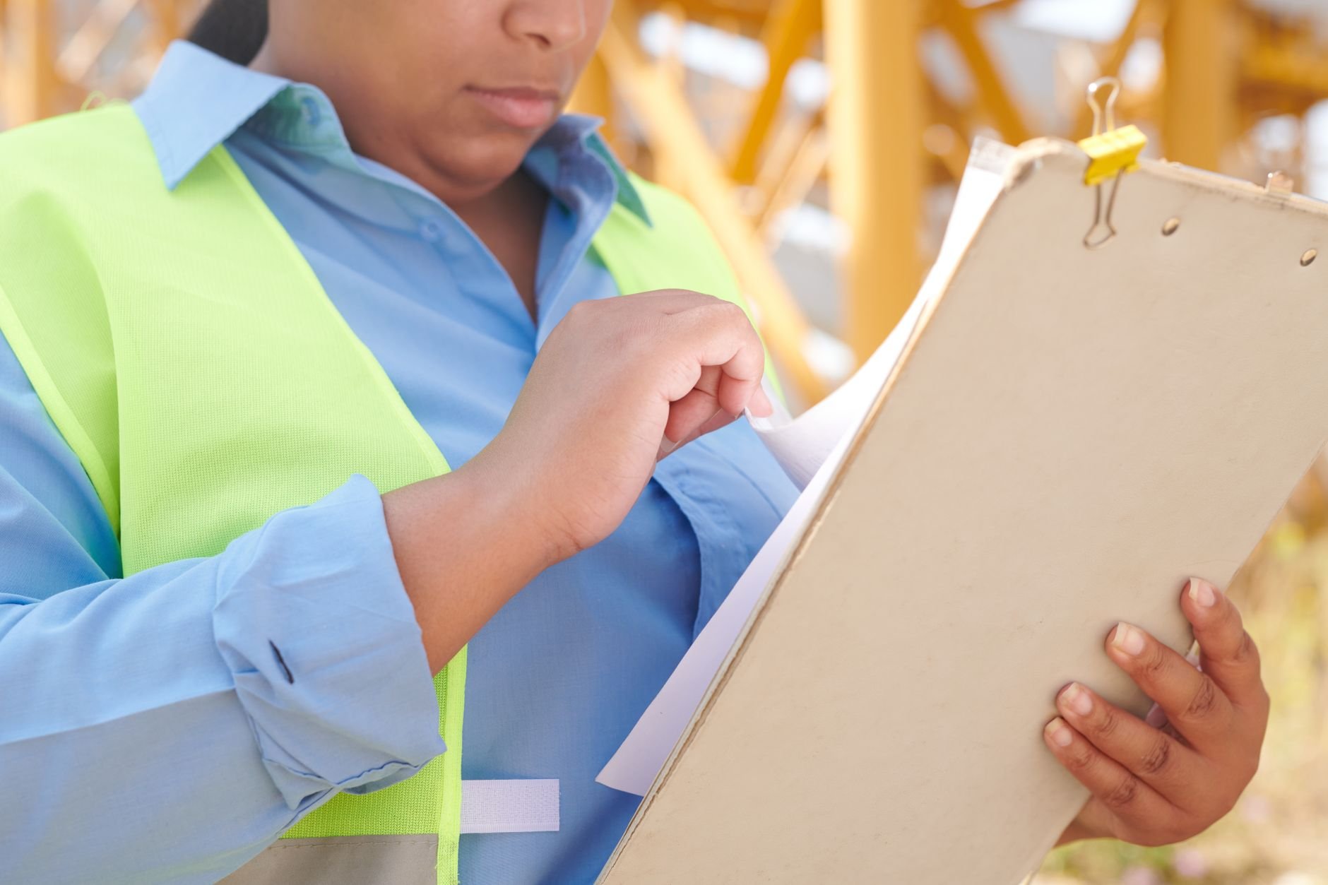 A female engineer in safety gear reviewing documents on a clipboard at a construction site